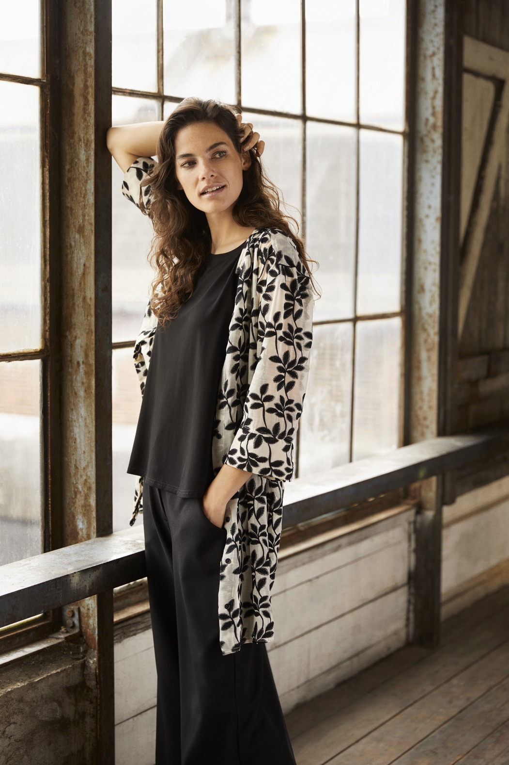 Model steht am Fenster und trägt ein Blusenkleid lange Bluse in weiss bestickt mit schwarzen Ranken von der Modemarke Masai Clothing Company